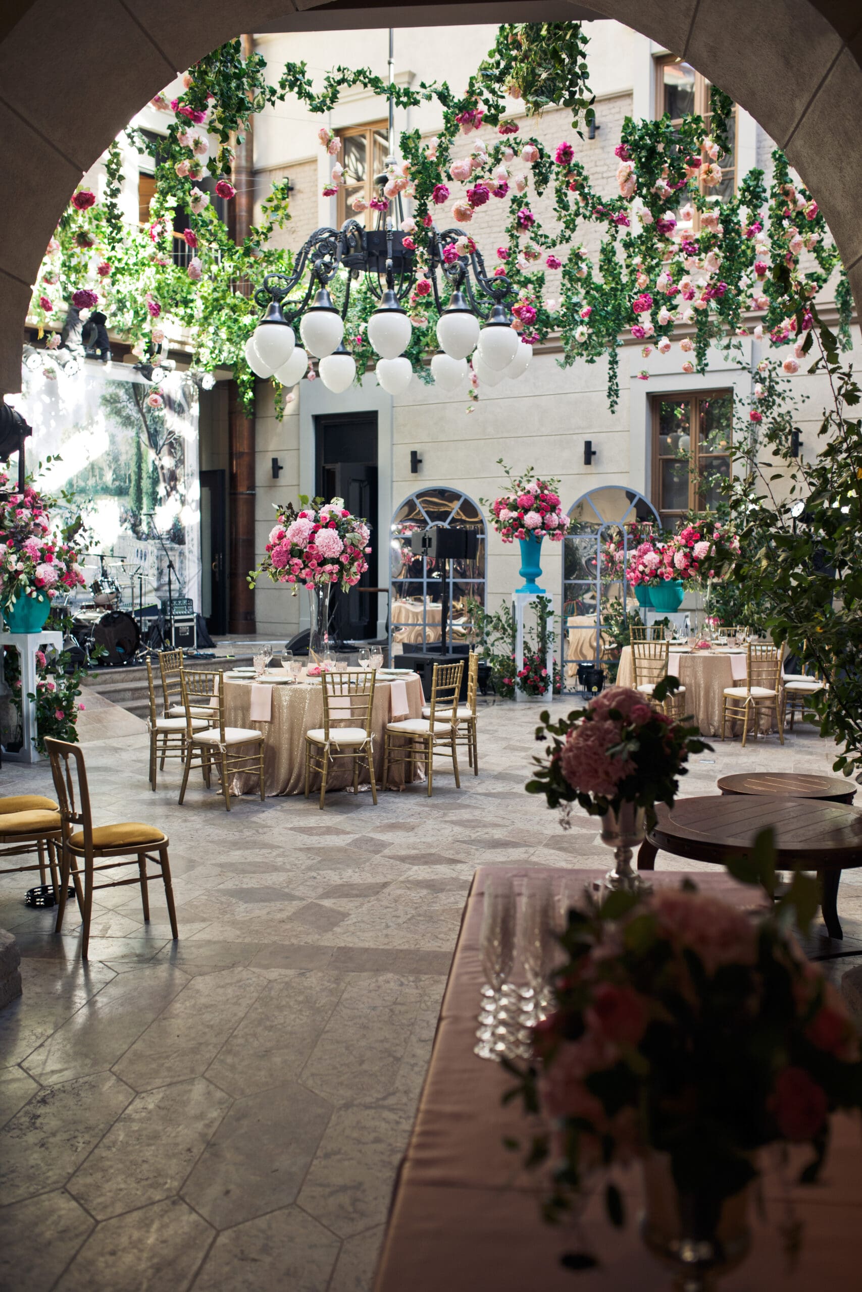 Courtyard Wedding Reception Decor with Hanging Florals Elegant outdoor courtyard wedding reception with pink floral centerpieces and overhead greenery installation
