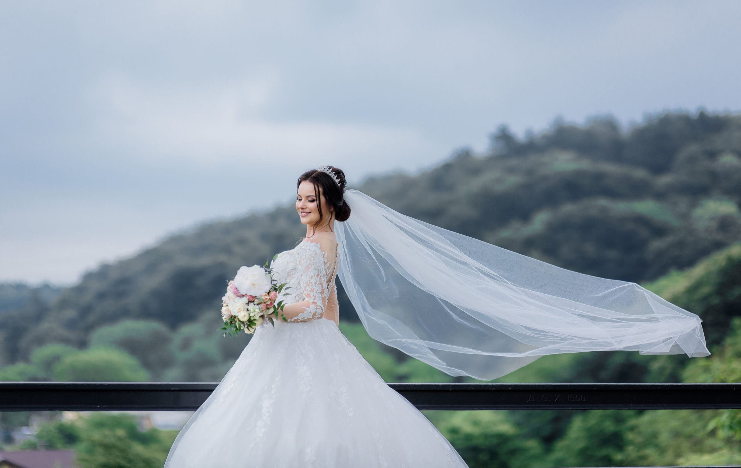 Bride in cathedral veil on windy hilltop Row of wooden wedding ceremony chairs decorated with white flowers and ribbon