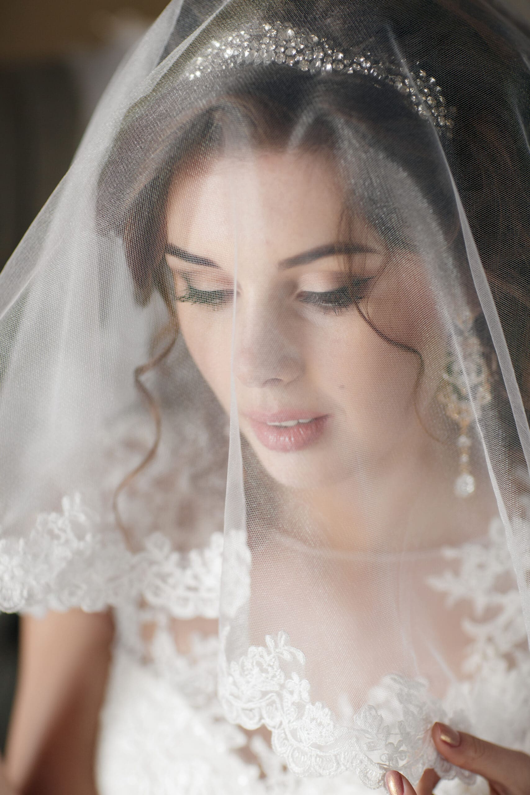 Bride Wearing Lace-Trimmed Wedding Veil Indoors Bride wearing a lace-trimmed wedding veil over her face, standing indoors with soft natural light