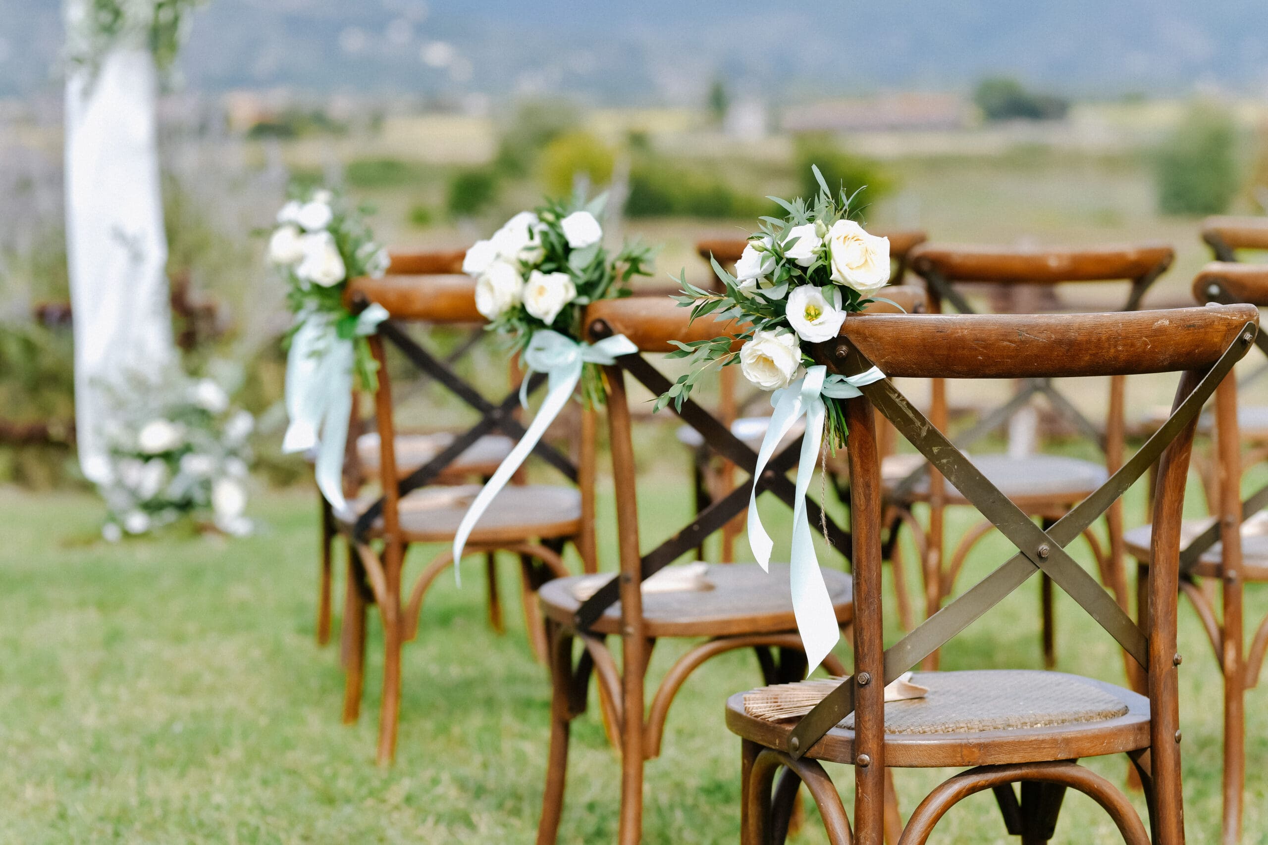 Outdoor Ceremony Chairs Decorated with White Flowers Row of wooden wedding ceremony chairs decorated with white flowers and ribbon